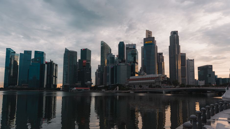 Dramatic skyline of Singapore reflecting on waterfront at dusk with towering skyscrapers.