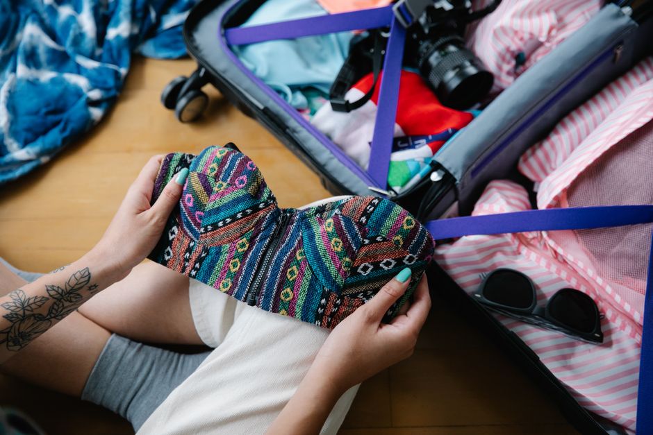 A woman packing a colorful bikini into a suitcase, preparing for her vacation trip.