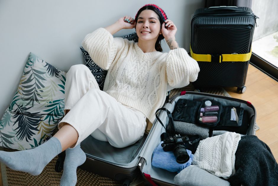 Young woman smiling while packing a suitcase for travel indoors.